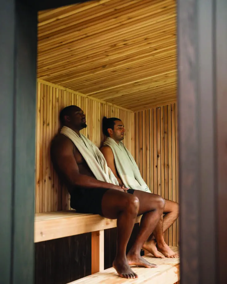 Two people resting in a timber sauna, towels around their necks